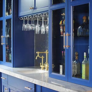 A bar with royal blue custom cabinetry fitted with lucite and polished brass door handles and drawer pulls.