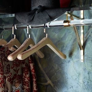 Close up shot of the clear acrylic rod attached to the lucite shelf with brass brackets, used for hanging clothes and displaying accessories.