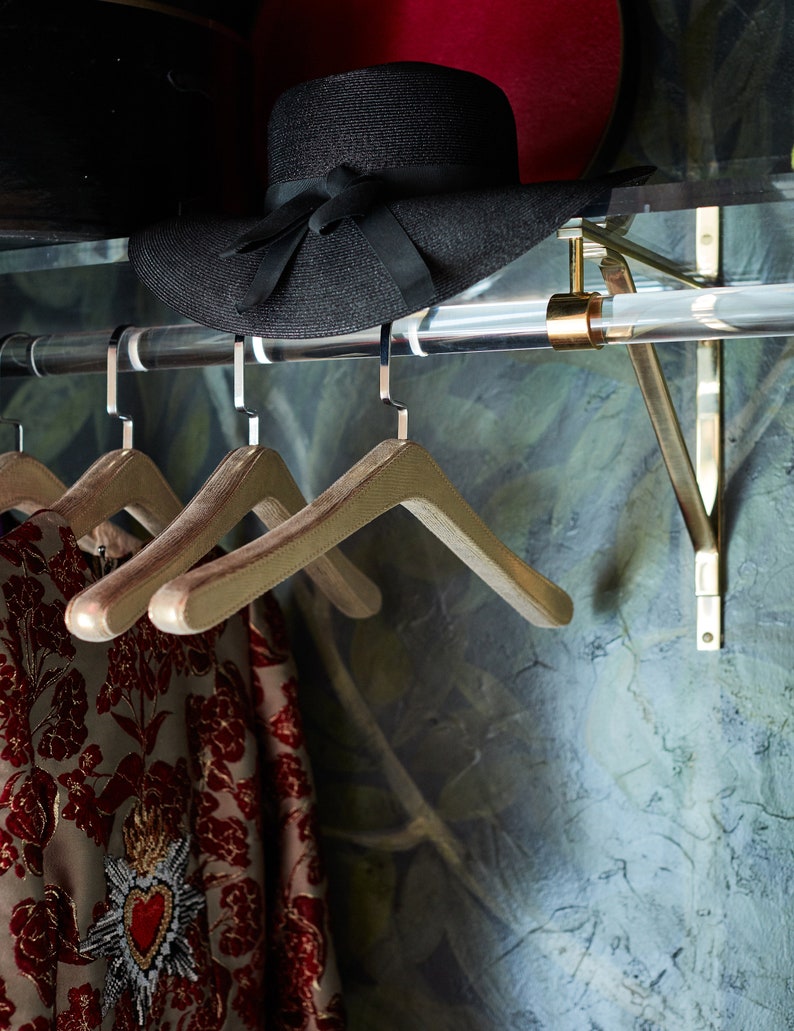Close up shot of the clear acrylic rod attached to the lucite shelf with brass brackets, used for hanging clothes and displaying accessories.