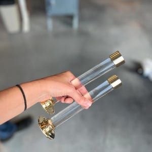 Wall mounted clear acrylic lucite cylindrical tube with polished brass end cap and hardware used for clothes hangers in a retail shop to display dresses.