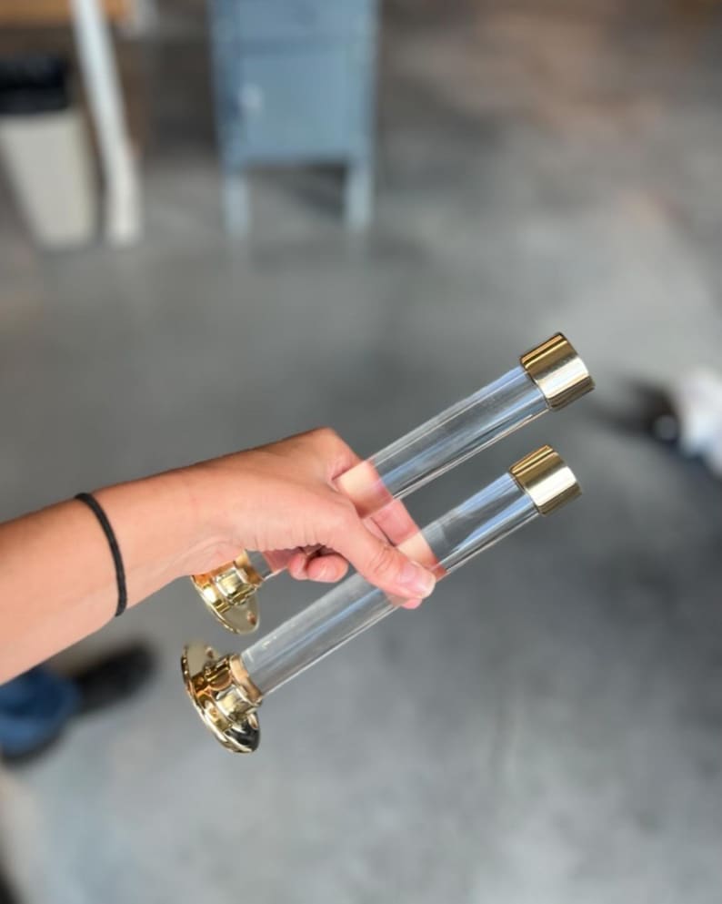 Wall mounted clear acrylic lucite cylindrical tube with polished brass end cap and hardware used for clothes hangers in a retail shop to display dresses.
