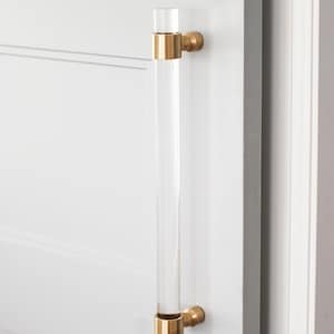 May include: A clear acrylic door handle with gold metal accents. The handle is mounted on a white door.