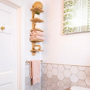 A corner of a bathroom featuring wood shelving and a lucite and brass towel rod, holding a light pink hand towel.