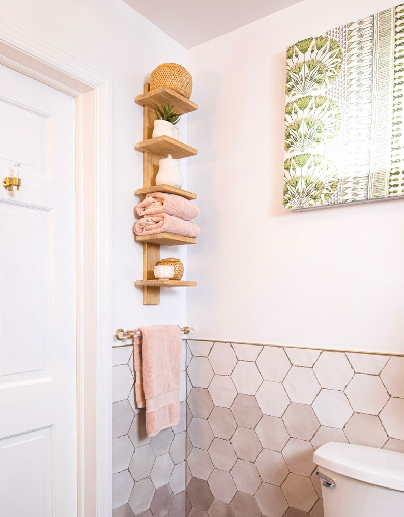 A corner of a bathroom featuring wood shelving and a lucite and brass towel rod, holding a light pink hand towel.