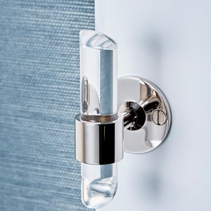 Cylindrical clear lucite piece with angled ends, inserted in a brass ring and wall mounted to be used as a robe or towel hook. Finish shown is chrome.