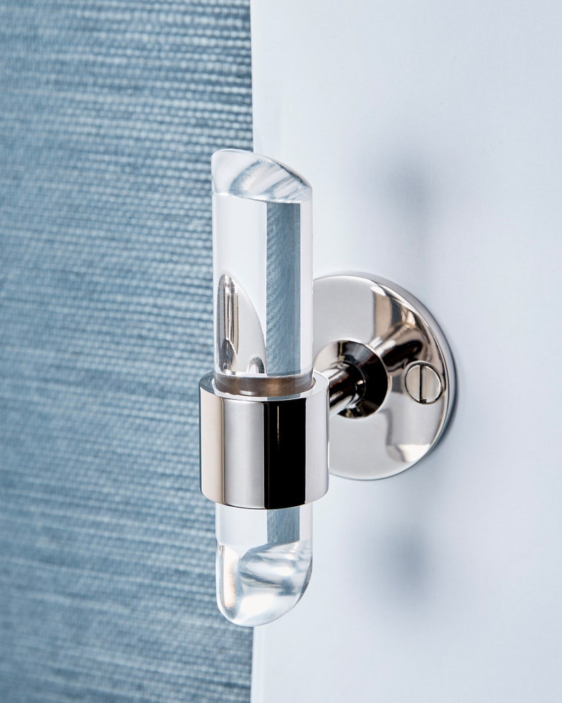 Cylindrical clear lucite piece with angled ends, inserted in a brass ring and wall mounted to be used as a robe or towel hook. Finish shown is chrome.