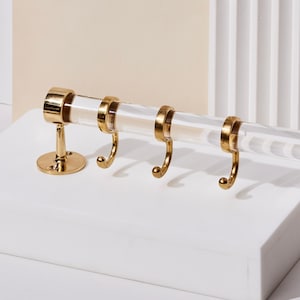 a pair of gold - plated hooks hang on a white surface