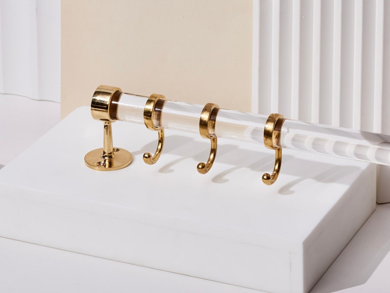 a pair of gold - plated hooks hang on a white surface