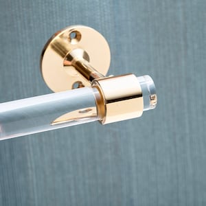 Detail shot of polished brass hardware ring fitted around a acrylic rod to be used as a wall mounted toilet paper holder.