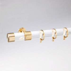 Round acrylic drapery rod with round polished brass end cap with matching round curtain rings.