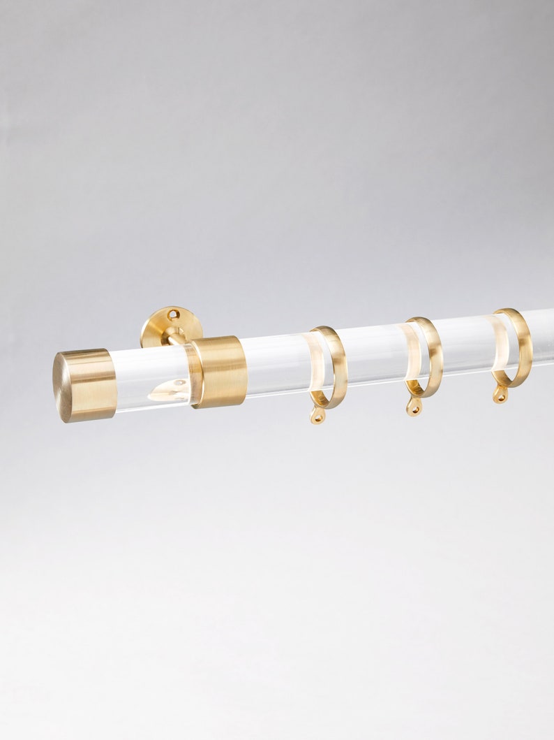 Round acrylic drapery rod with round polished brass end cap with matching round curtain rings.
