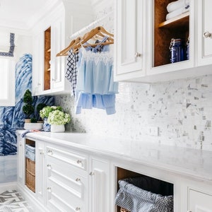 Large white laundry room featuring a clear acrylic rod, installed between two sets of upper cabinets, used to hang clean laundry to dry.