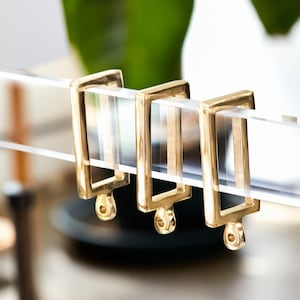 Three gold polished brass rectangular curtain rings on a clear lucite rod.
