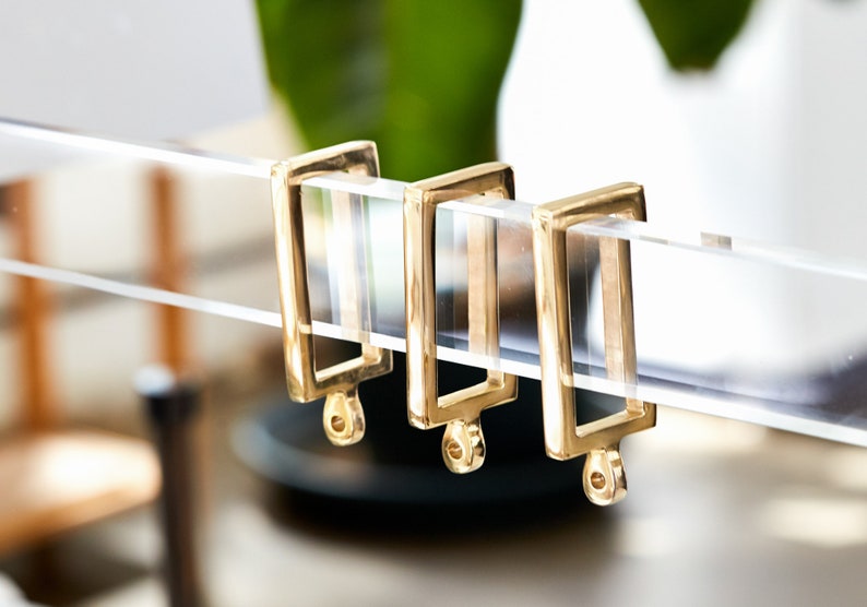 Three gold polished brass rectangular curtain rings on a clear lucite rod.