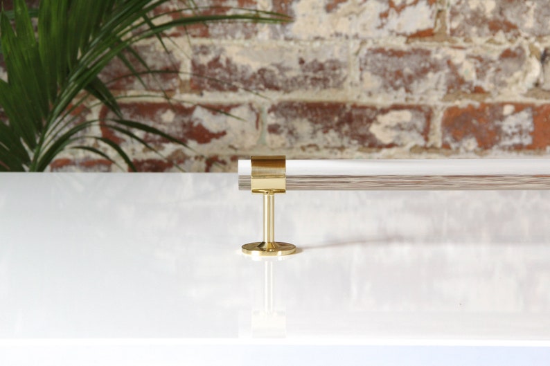 A clear lucite rod fitted into a brass ring with mounting hardware attached, finished in satin nickel, to be used as a towel bar.