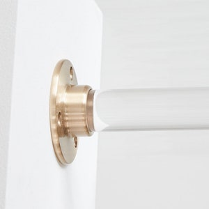 Close up detail of satin brass hardware and lucite acrylic rod attached to white wall.