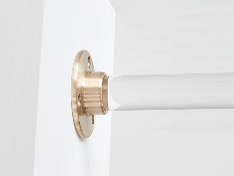 Close up detail of satin brass hardware and lucite acrylic rod attached to white wall.