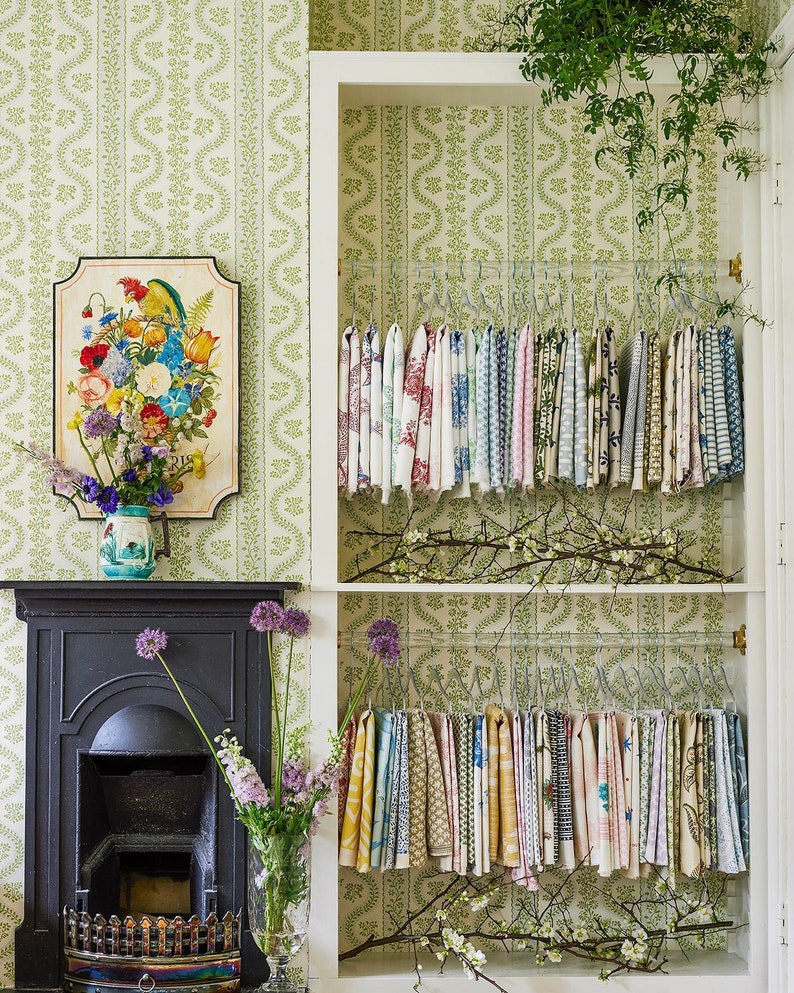 Clear lucite rods installed in a closet, featuring sage green patterned wallpaper, used to hang fabric samples.