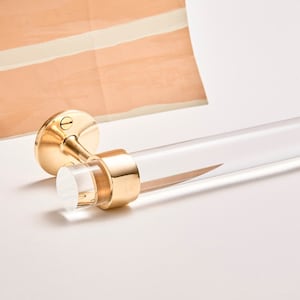A clear lucite rod fitted into a brass ring with mounting hardware attached, finished in satin brass, to be used as a towel bar.