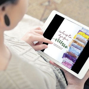 May include: A person is using a white tablet displaying a page titled "colors to dye for." The page features a stack of colorful fabric samples. The tablet is being held in the person's hands.
