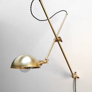 May include: A brass wall-mounted lamp with a black cord and a dome-shaped shade. The lamp has a flexible arm that can be adjusted to direct the light.