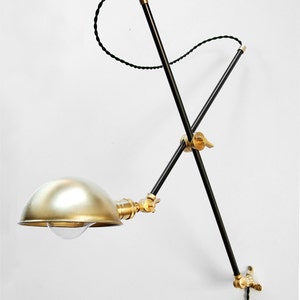 May include: A black and brass adjustable wall lamp with a gold-colored dome shade. The lamp has a black cord and a brass switch.