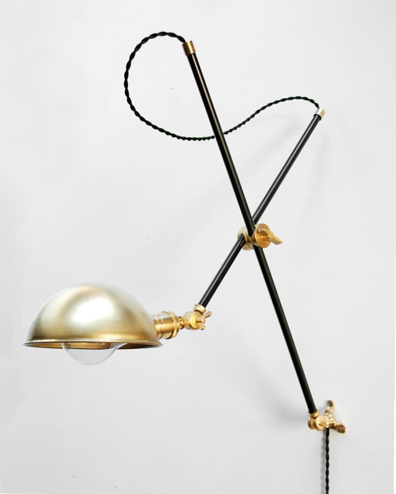 May include: A black and brass adjustable wall lamp with a gold-colored dome shade. The lamp has a black cord and a brass switch.