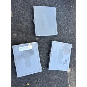 May include: Three rectangular light gray plastic storage cases with metal latches and hinges. Two cases feature handwritten white labels, one reading "Mustard Oil 2009" and the other "New Mouse Section," while the third case remains unlabeled.