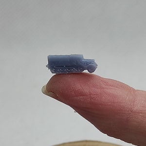 Könnte beinhalten: Ein kleines, hellblaues, Plastikmodell eines Militärlastwagens. Der LKW befindet sich auf einem Finger, und der Finger ruht auf einer Holzoberfläche.
