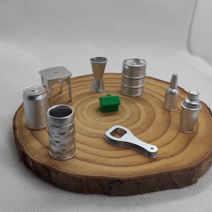 May include: A set of miniature silver-colored barware items, including a bottle opener, a shaker, a can, a stool, a shot glass, a bottle, and a barrel, arranged on a wooden circular base.