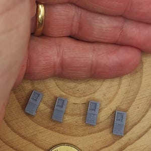 Puede incluir: Cuatro objetos rectangulares pequeños y grises con un diseño detallado se muestran sobre una superficie de madera. También hay una moneda de 10 céntimos de euro. Los objetos parecen ser modelos arquitectónicos en miniatura.