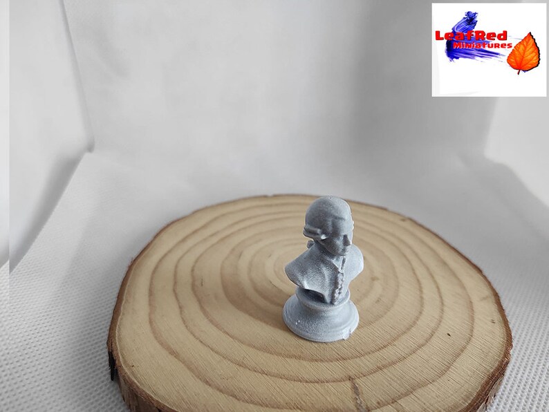 May include: A gray bust sculpture of a person with a hat on a wooden base. The bust is on a wooden surface.