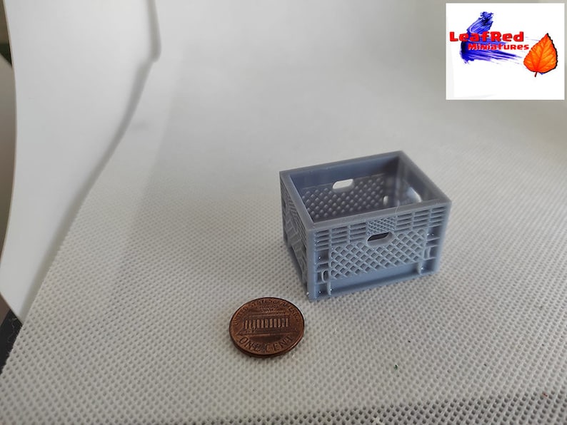 May include: A miniature gray plastic crate, approximately the size of a US penny, for use in dollhouses or model railroad layouts.