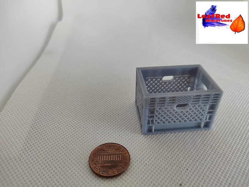 May include: A gray plastic crate, approximately 2 inches tall, next to a US penny. The crate has a grid pattern and is made for holding small items.