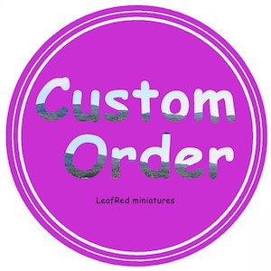 Puede incluir: Una taza de cerámica blanca con asa negra y el texto "But First, Coffee" en negrita negra. La taza se encuentra sobre un fondo borroso, sugiriendo un ambiente acogedor.