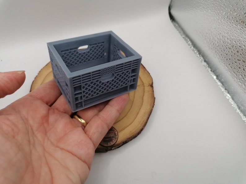 May include: A small, gray plastic crate with a grid pattern. The crate is empty and is sitting on a wooden surface.