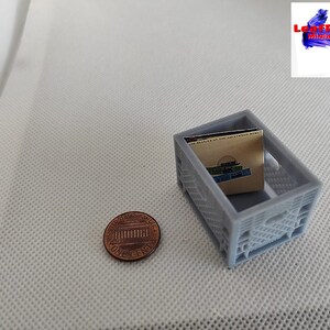 May include: A gray plastic crate with a small stack of paperbacks inside. The crate is about the size of a penny.