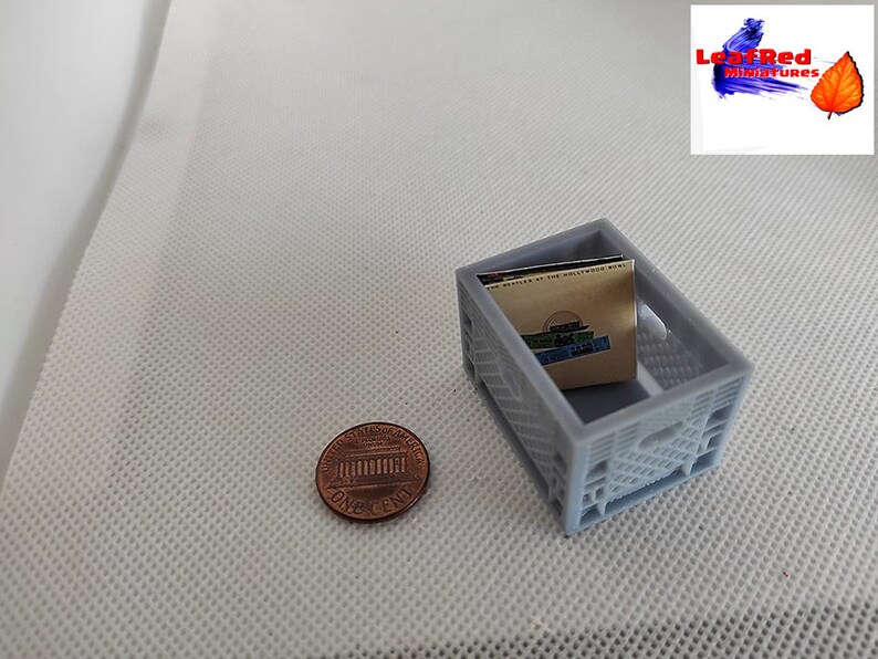 May include: A gray plastic crate with a small stack of paperbacks inside. The crate is about the size of a penny.