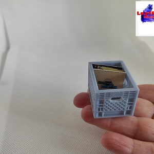 May include: A miniature gray plastic crate with a blue and white pattern, holding two miniature books. The crate is about 2 inches tall.