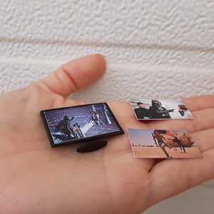 Op de afbeelding: Een zwarte miniatuurtelevisie met een sc&egrave;ne uit Star Wars die op het scherm wordt afgespeeld. Twee kleine foto's van sc&egrave;nes uit Star Wars zijn ook in de afbeelding.