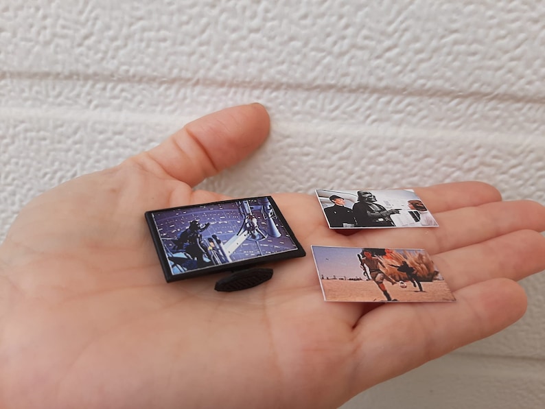 Op de afbeelding: Een zwarte miniatuurtelevisie met een sc&egrave;ne uit Star Wars die op het scherm wordt afgespeeld. Twee kleine foto's van sc&egrave;nes uit Star Wars zijn ook in de afbeelding.