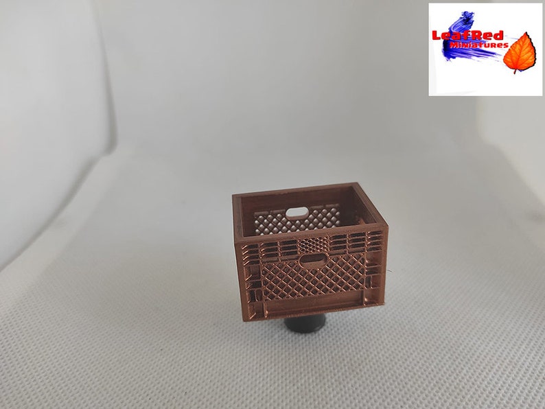 May include: A miniature brown plastic crate with a grid pattern. The crate is about 1 inch tall and 1 inch wide.