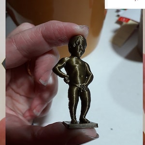 May include: A 3D printed bronze-coloured figurine of a small child standing with their hands on their hips. The figurine is on a small square base.