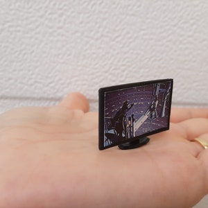 Op de afbeelding: Een miniatuur zwart televisietoestel met een scherm dat een sc&egrave;ne uit een sciencefictionfilm laat zien. De televisie ligt op de hand van een persoon.