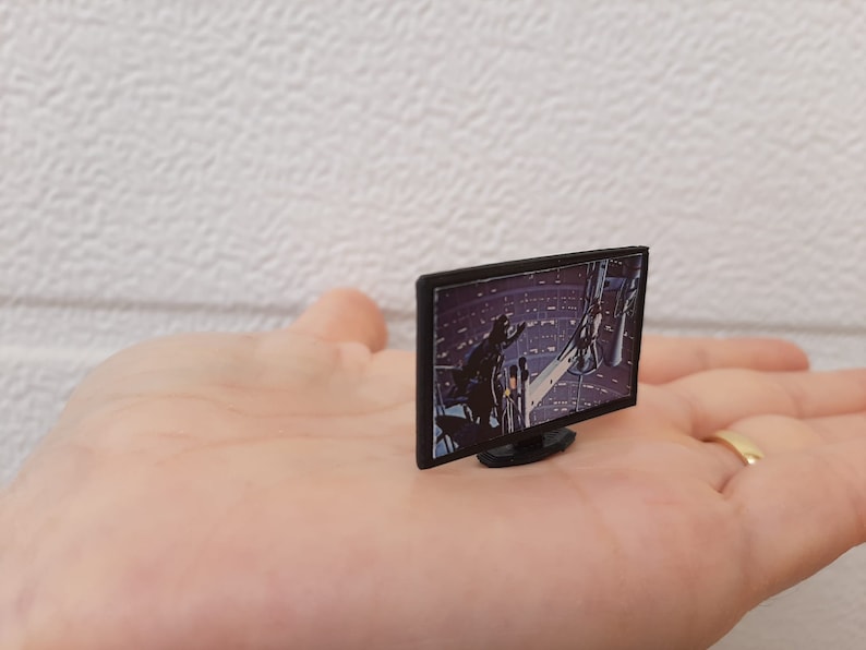 Op de afbeelding: Een miniatuur zwart televisietoestel met een scherm dat een sc&egrave;ne uit een sciencefictionfilm laat zien. De televisie ligt op de hand van een persoon.