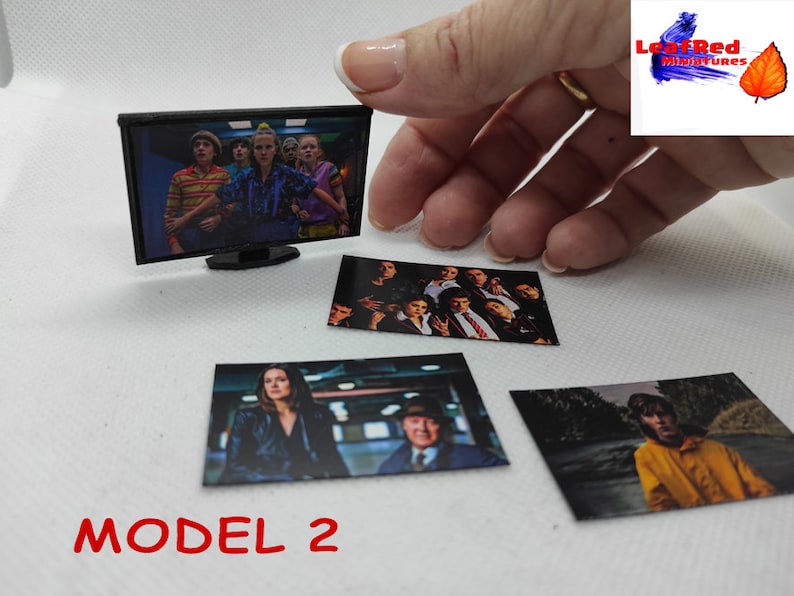 Op de afbeelding: Een miniatuurtelevisie met een zwart frame en een scherm waarop een groep mensen te zien is. Er liggen vier kleinere foto's van mensen op een wit oppervlak. De tekst "MODEL 2" is op het oppervlak gedrukt.