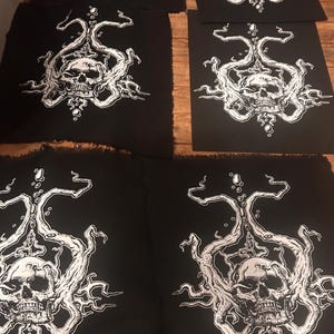 Op de afbeelding: Verschillende zwarte stoffen patches met een wit schedelontwerp. De schedel is omgeven door ingewikkelde, wervelende witte lijnen en vormen. De patches zijn rechthoekig met een gerafelde rand.