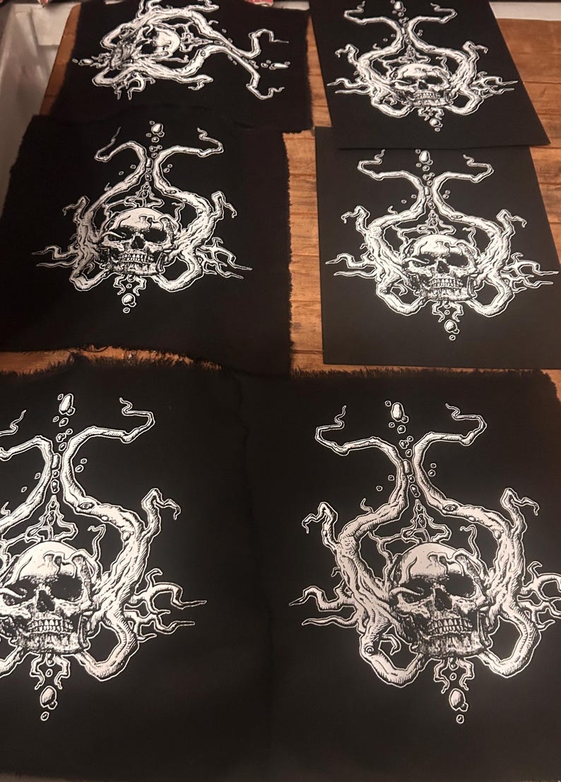 Op de afbeelding: Verschillende zwarte stoffen patches met een wit schedelontwerp. De schedel is omgeven door ingewikkelde, wervelende witte lijnen en vormen. De patches zijn rechthoekig met een gerafelde rand.