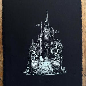 May include: A rectangular black fabric patch featuring a white screen-printed illustration of a gothic mansion with tall spires, bare trees, and a gated entrance. The design includes small flying bats and tombstones, with raw, frayed edges.