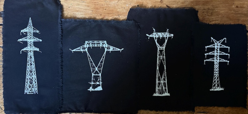 Op de afbeelding: Vier rechthoekige zwarte stoffen patches met gerafelde randen, elk voorzien van een witte zeefdrukillustratie van een ander type elektriciteitsmast. De ontwerpen tonen ingewikkelde roosterstructuren van diverse mastvormen.